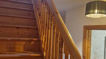 A wooden staircase with a handrail, a ceiling light fixture, and a door in the background.