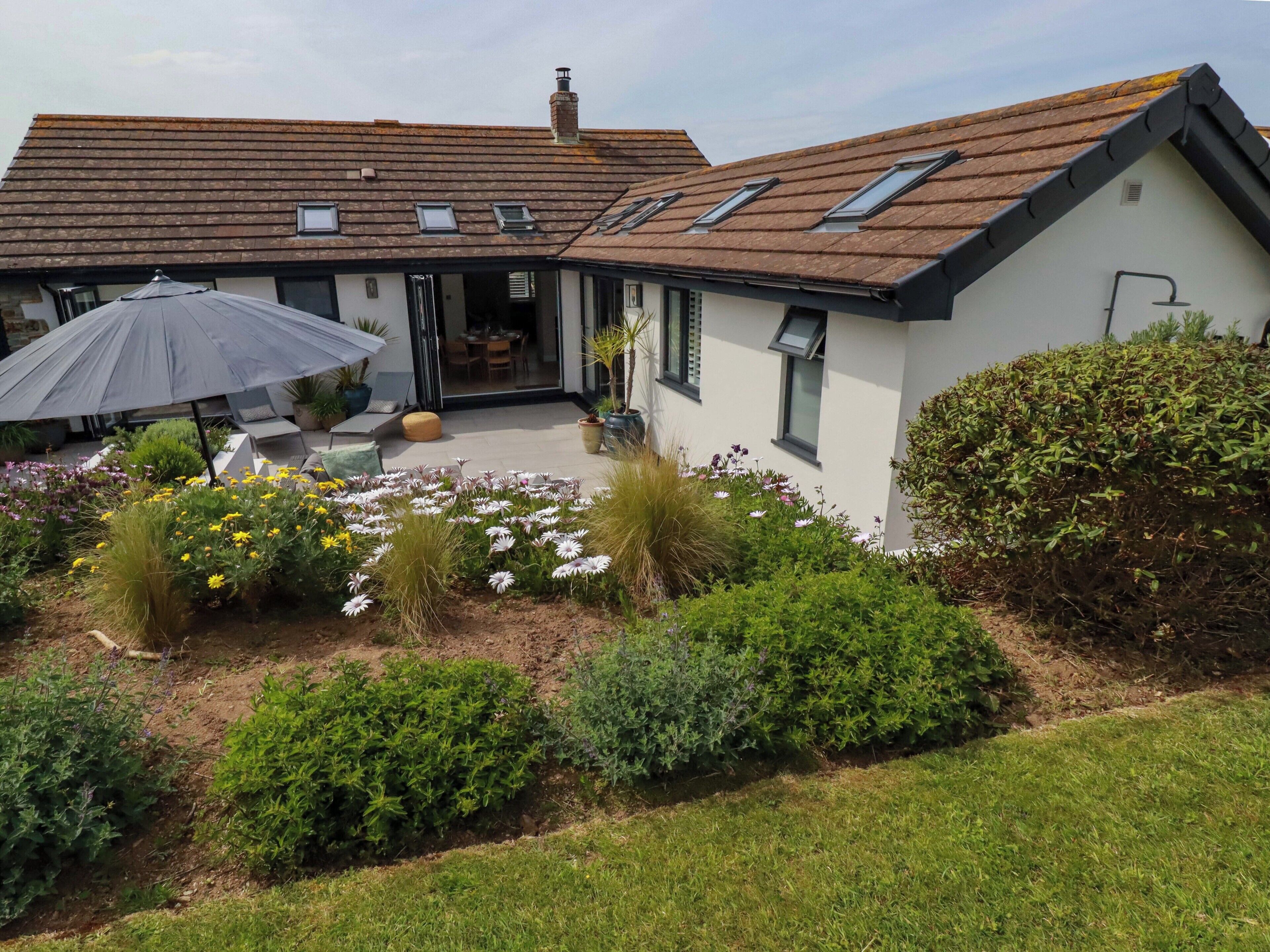 A house with a sloped roof, skylights, a covered patio, and a garden with various plants and flowers.