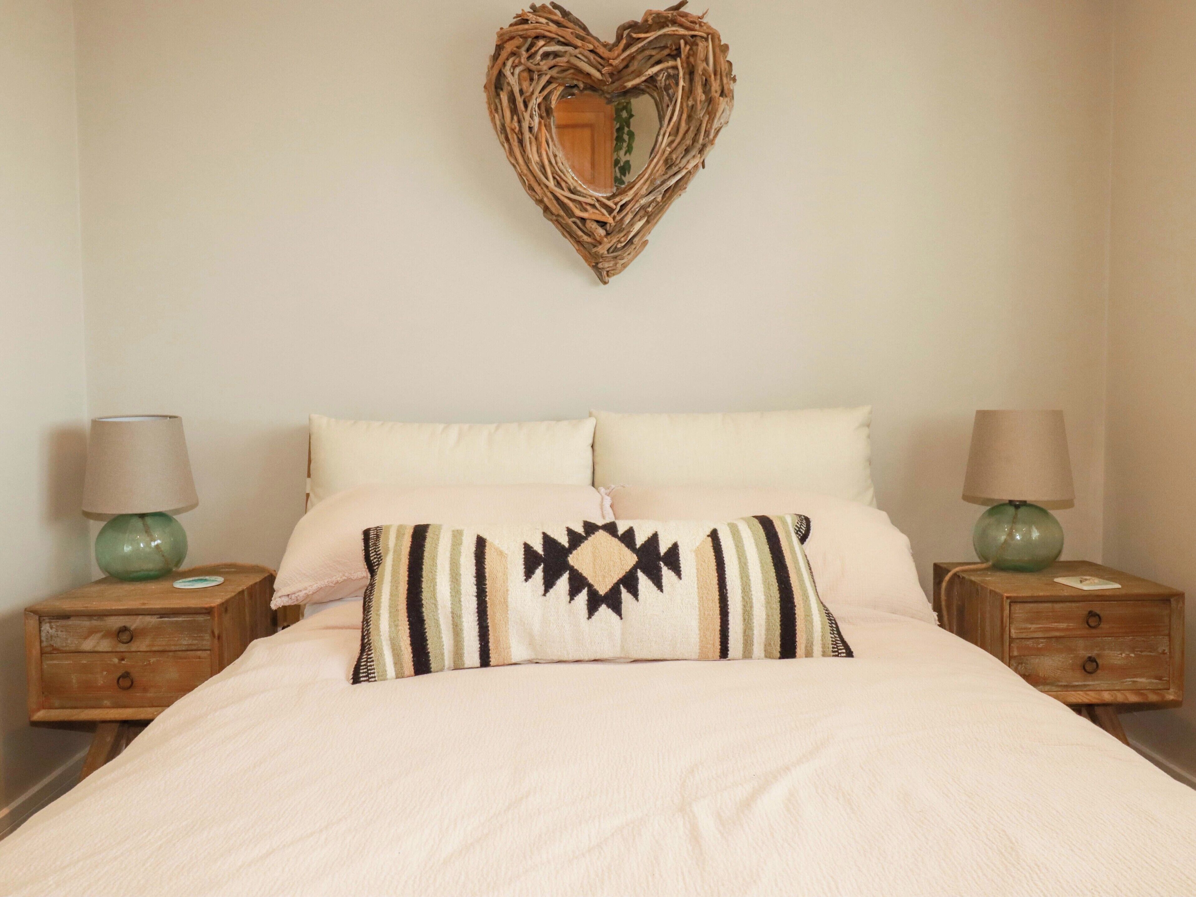 A bedroom with a bed, two nightstands, a heart-shaped wall decoration, and two lamps.