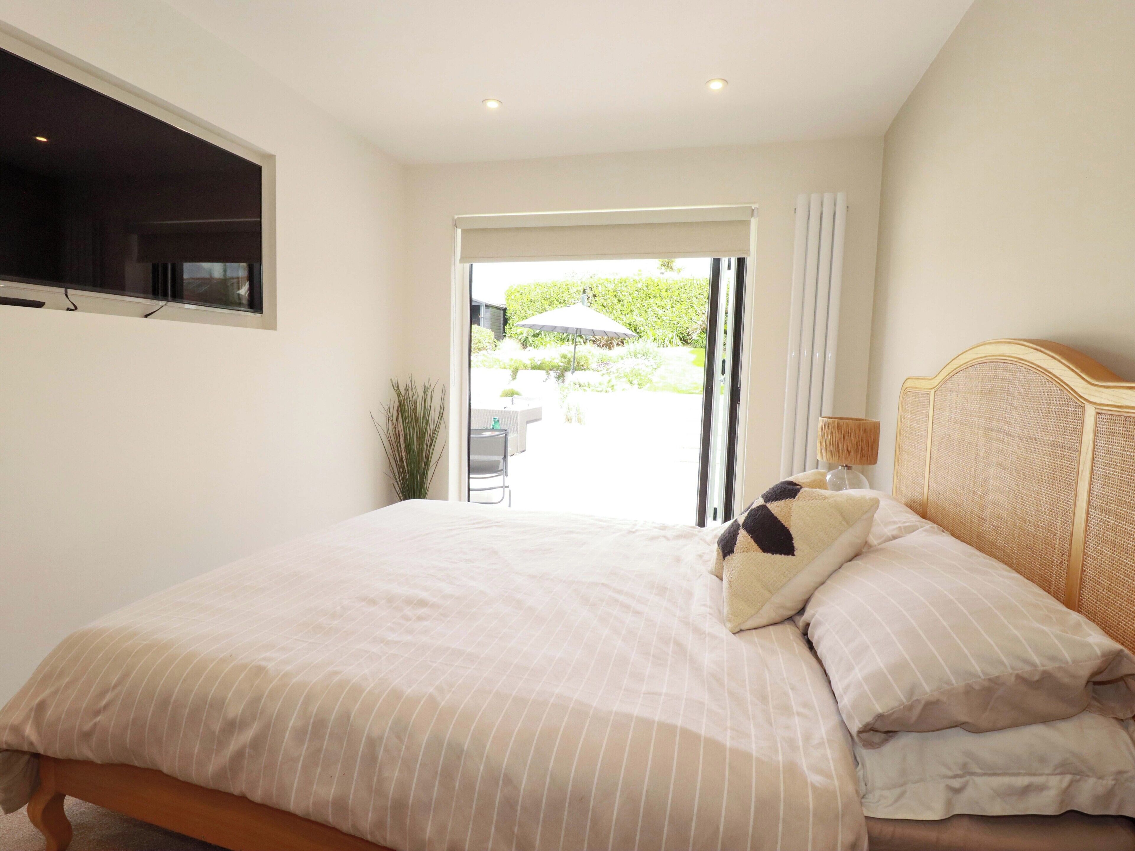 A bedroom with a bed, a window, a door leading to an outdoor area, and a small table with a chair.