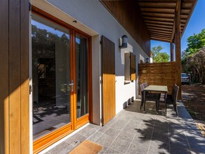 A modern house with large sliding glass doors, a covered patio with a table and chairs, and a wooden fence. - Apartment in Lacanau Near Beach (Lacanau)