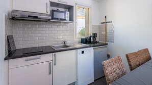 A compact kitchen with white cabinetry, a built-in microwave, a coffee maker, and a dishwasher. - Apartment in Lacanau Near Beach (Lacanau)