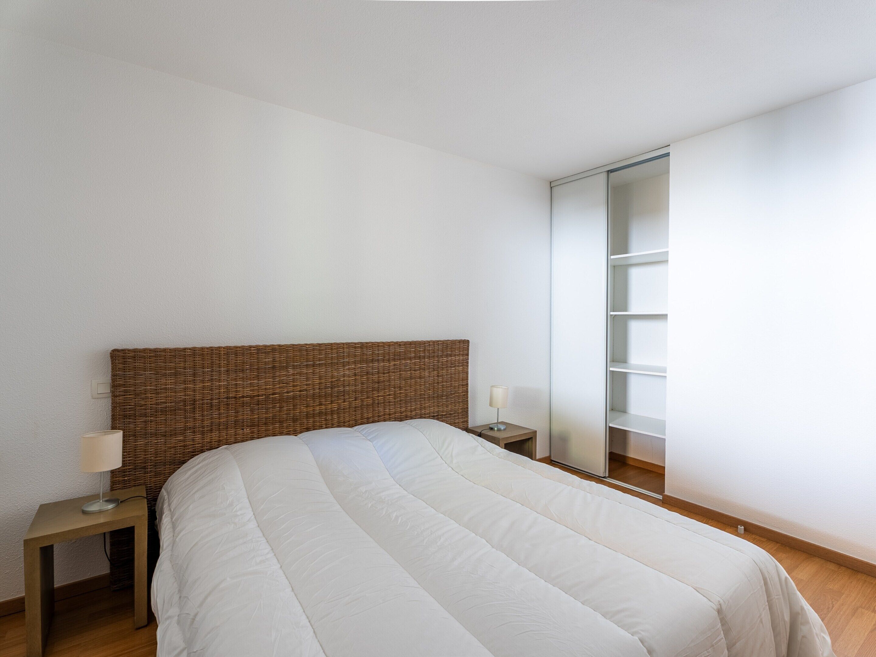 Un dormitorio con una cama grande, una mesita de noche, una lámpara, un cabecero de mimbre y un armario con espejo.
