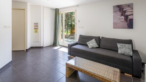 A modern living room with a grey sofa, a small coffee table, and a glass door leading to a garden. - Apartment in Lacanau Near Beach (Lacanau)