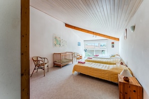 Una habitación con dos camas, una cuna, una silla y una viga de madera en el techo.