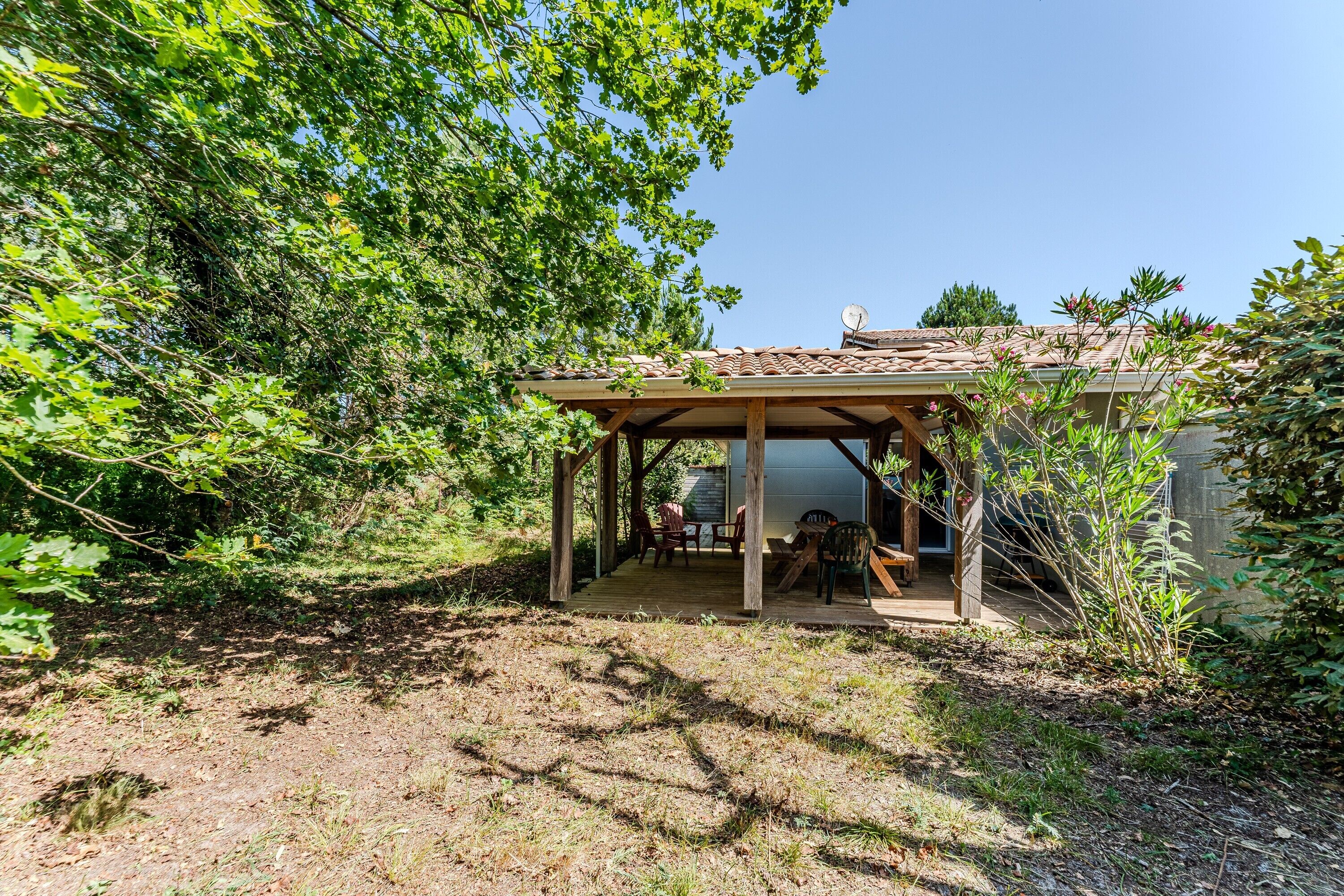 Un área de estar al aire libre cubierta con una mesa y sillas, rodeada de árboles y un edificio.