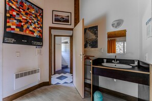 A hotel room with a bathroom featuring a sink, mirror, and a poster on the wall.