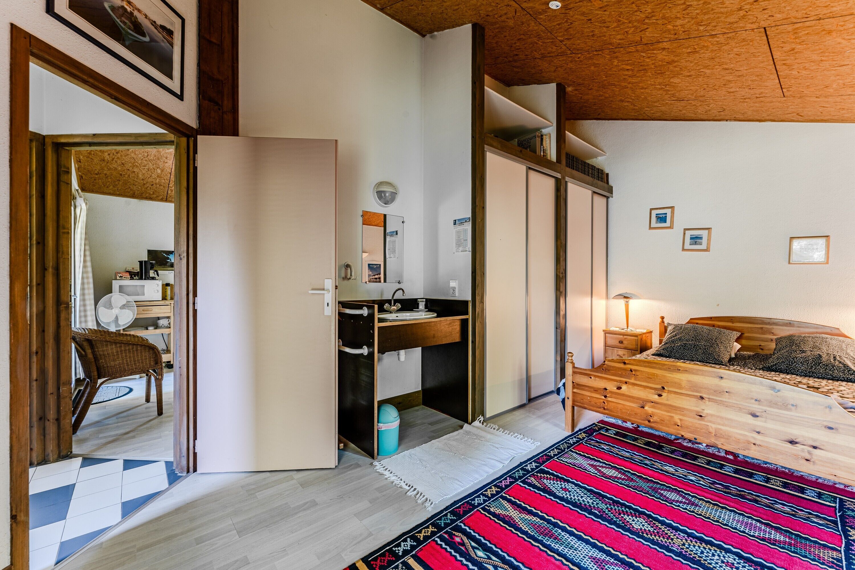 Ein Schlafzimmer mit einem Holzbett, einem Schreibtisch mit Spiegel, einem Stuhl und einem gemusterten Teppich.