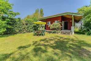 Un bâtiment rouge avec un toit vert, un patio couvert avec une table et des chaises, et un parasol jaune.