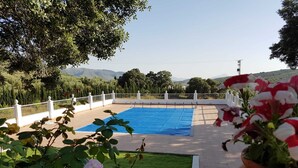 Une piscine recouverte d’une bâche bleue, entourée d’une clôture blanche, avec de la verdure et une vue sur des collines lointaines.
