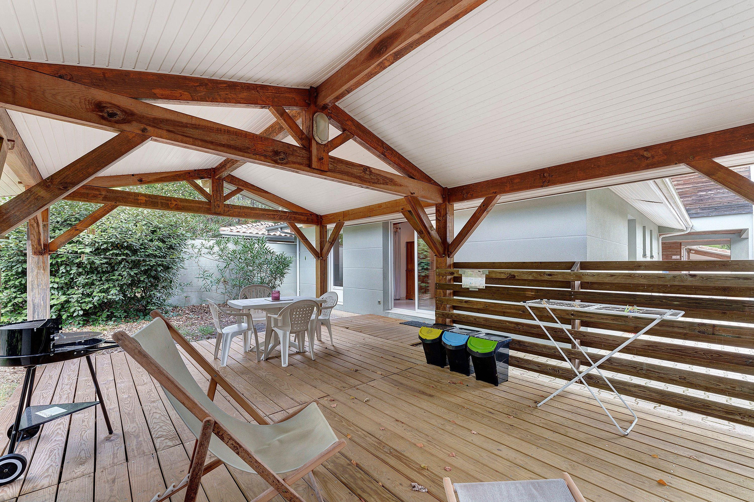 Eine überdachte Terrasse im Freien mit Holzbalken, einem Tisch mit Stühlen und einer Bank.