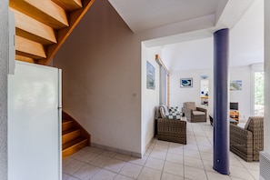 Un vaste espace de vie comprenant un escalier, des meubles en osier et une grande colonne.