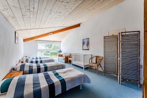 Ein Zimmer mit zwei Betten, einem Babybett, einem Sessel, einer Heizung und einem Fenster.