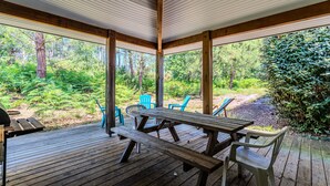 A covered outdoor area with a wooden deck, picnic table, and chairs, surrounded by lush greenery and trees. - Apartment "Chott" for 6 in Sanguinet with Terrace (Sanguinet)