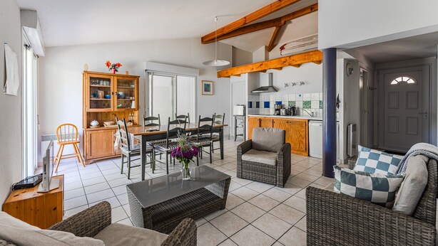 A spacious living area with a dining table, wicker furniture, and a kitchen in the background. - Apartment "Chott" for 6 in Sanguinet with Terrace (Sanguinet)