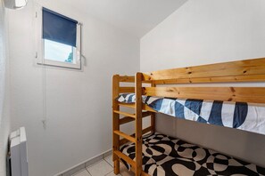 A bunk bed with a wooden ladder, a window with a blue blind, and a patterned bedspread. - Apartment '4p Sanguinet-Doum Doum' with Outdoor Space (Sanguinet)
