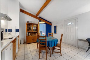 A dining area with a table set for two, wooden chairs, a blue tablecloth, and a kitchen area with cabinets and a sink. - Apartment '4p Sanguinet-Doum Doum' with Outdoor Space (Sanguinet)
