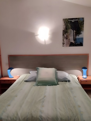 Un dormitori amb un llit, dues làmpades de nit, un reposacapses i un quadre penjat a la paret.