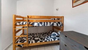 En våningssäng med ett rutmönstrat madrass och en träram i ett rum med vita väggar och ett kaklat golv.