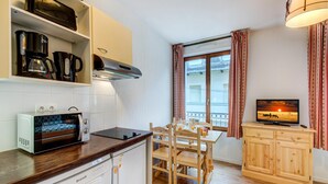 Una cucina compatta con forno a microonde, tostapane e macchina del caffè, un tavolo da pranzo in legno con sedie, una televisione e una finestra con tende.