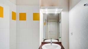 Un bagno con piastrelle bianche e gialle, un mobile lavabo in legno, un lavandino bianco e uno specchio.