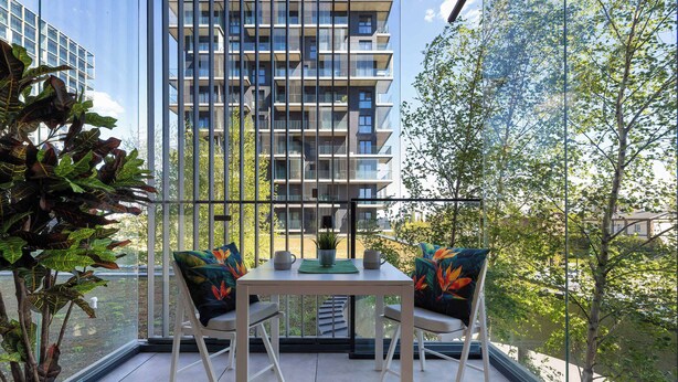 Uma varanda com mesa e cadeiras, um vaso de planta e vista para um edifício alto.