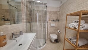 Un bagno moderno con doccia vetrata, lavandino bianco, servizi igienici e mensola in legno con asciugamani.