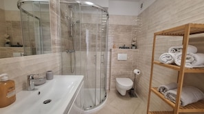 Ein modernes Badezimmer mit einer Duschkabine, einem weißen Waschbecken, einer Toilette und einem Holzregal mit Handtüchern.