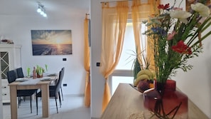 Ein Essbereich mit einem für zwei gedeckten Tisch, einem Sonnenuntergangsbild an der Wand und einer Vase mit Blumen auf dem Tisch.