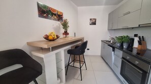 Eine kompakte Küche mit Holzarbeitsplatte, einem schwarzen Stuhl, einer Obstschale, einem Blumentopf und Edelstahlgeräten.