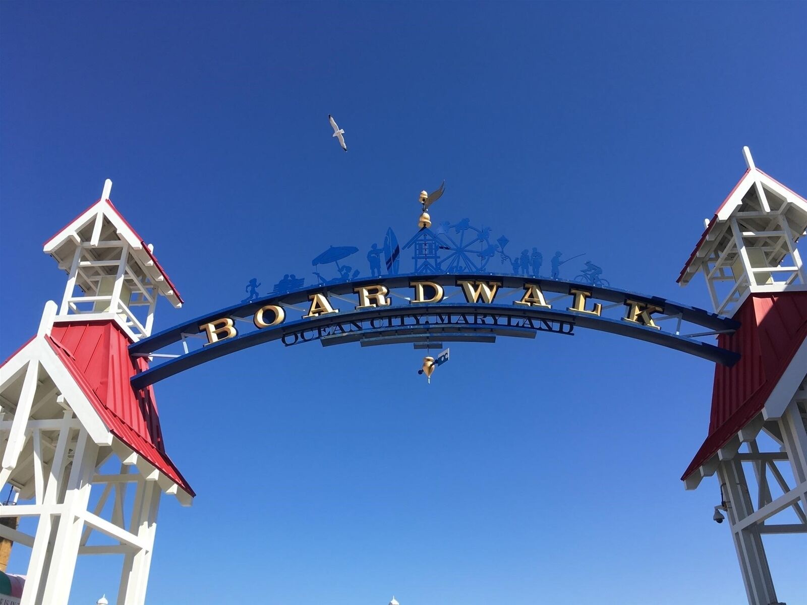 Un letrero que dice 'Boardwalk', flanqueado por dos torres blancas con techos rojos.
