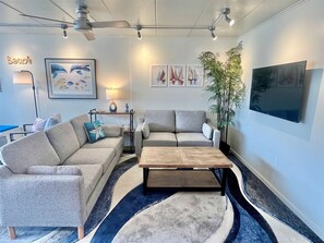 A modern living room with two grey sofas, a wooden coffee table, and a large TV on the wall. - New for 2026! Quick walk to the beach! Sleeps 6, Parking for two (Ocean City)