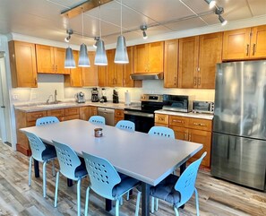 A modern kitchen with wooden cabinets, stainless steel appliances, and a central island with chairs. - New for 2026! Quick walk to the beach! Sleeps 6, Parking for two (Ocean City)