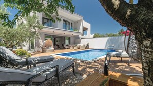 Ein modernes Haus mit Swimmingpool, Gartenmöbeln und einem Baum.