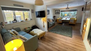 Ein Wohnzimmer mit einer Couch, einem kleinen Tisch, einer Lampe und einem an der Wand befestigten Fernseher.