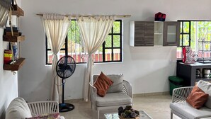 Una sala de estar con techo de madera, sofás blancos, una mesa de centro de vidrio y un ventilador.