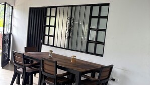 Un comedor con una mesa y sillas de madera, una ventana con reja de metal y un altavoz fijado a la pared.