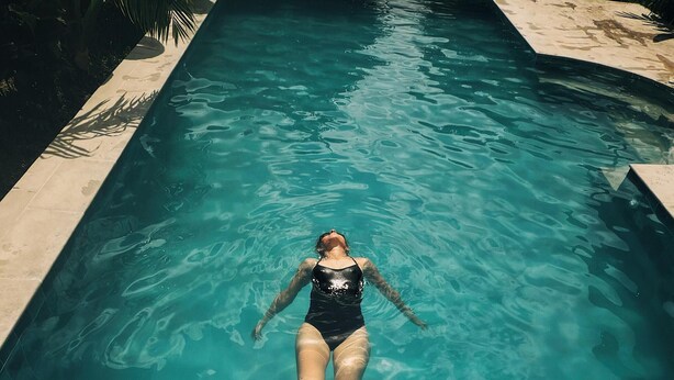 Una persona nadando en una piscina clara con borde de azulejos.
