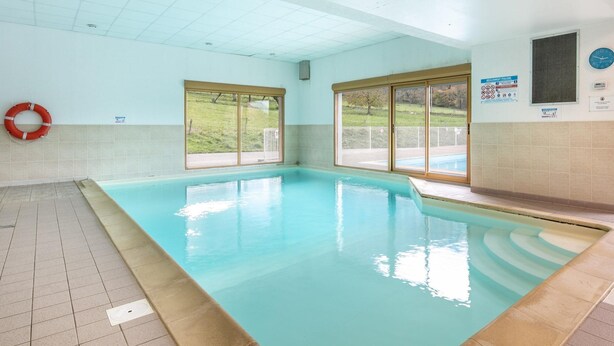 Une piscine intérieure avec des murs carrelés, une bouée de sauvetage et de grandes fenêtres.