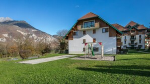 Un immeuble à plusieurs étages doté d’une façade en bois, d’un toit végétalisé et d’un espace de jeux pour enfants avec un toboggan.