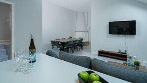 A modern living room with a dining area, a flat-screen TV mounted on the wall, and a staircase leading to another level.