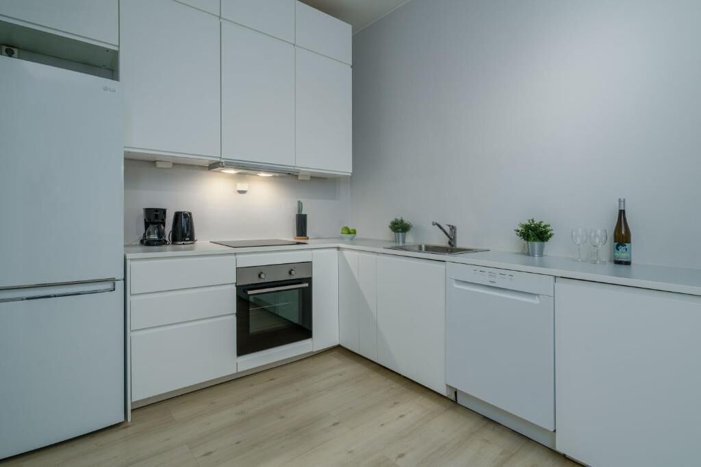 A modern kitchen with white cabinets, a built-in oven, a dishwasher, and a coffee maker.