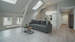 A modern loft apartment with skylights, a kitchenette, and a grey sofa.