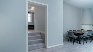 A modern interior with a staircase leading to another room, a dining area with a table and chairs, and light-colored walls and flooring.