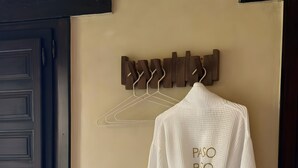A white robe hanging on a wooden hanger with 'PASO PASO' text, a dark door, and a beige wall. - Boutique rural casita Paso Paso met adembenemend bergzicht en prachtig zwembad (Torrox)
