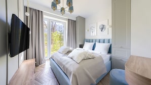Ein modernes Schlafzimmer mit einem großen Bett, einem Flachbildfernseher, Blick auf Bäume durch das Fenster und einem eingebauten Kleiderschrank.