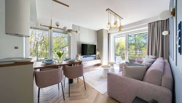 Ein modernes Wohnzimmer mit einer Couch, einem Essbereich mit Stühlen und einem Tisch, einem Flachbildfernseher und großen Fenstern mit Blick auf Bäume.