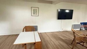 A room with a white table, two chairs, a television on the wall, and a laptop on a desk. - La Résidence du Moulin 304 - Comfortable and quiet studio in Jonzac (Jonzac)