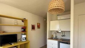 A compact living space with a kitchenette, a yellow shelving unit with electronic devices, and a woven pendant light. - La Résidence du Moulin 304 - Comfortable and quiet studio in Jonzac (Jonzac)