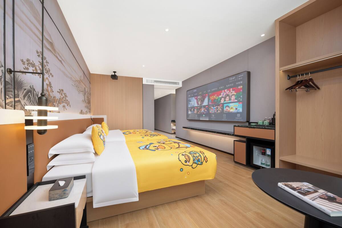 A modern hotel room with a large bed, a flat-screen TV, a desk, and a wardrobe.